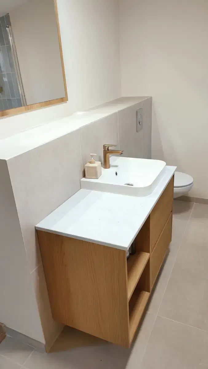 Meuble de salle de bain à finition bois avec vasque blanche, robinet chromé et miroir.